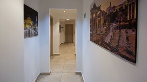 A hallway with a tiled floor, white walls, and two large framed pictures depicting historical architecture. - Aurelio Deluxe Rooms (Rome)