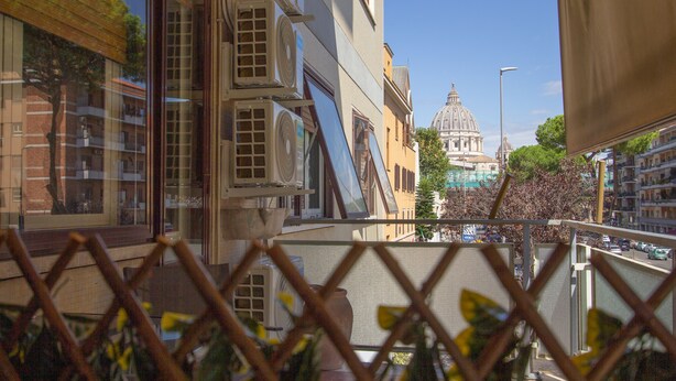 A view from a balcony with a metal fence, overlooking a street with buildings and a large dome structure in the background. - Aurelio Deluxe Rooms (Rome)