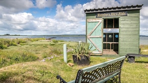 A rustic bird hide structure with a bench in front, overlooking a body of water.