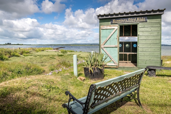A rustic bird hide structure with a bench in front, overlooking a body of water.