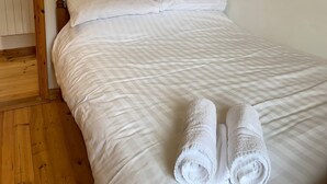Un lit simple avec une literie blanche et deux serviettes enroulées posées dessus.