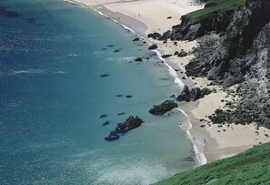 Vue aérienne d’une zone côtière avec une plage de sable, des affleurements rocheux et une eau d’un bleu limpide.