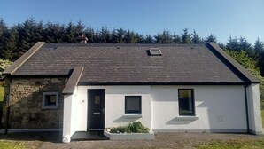 Une maison à deux étages, avec des fondations en pierre, un toit foncé et une façade blanche.