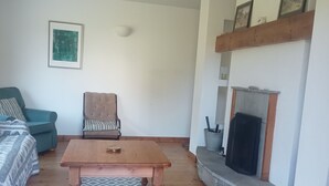 Un salon avec une table basse en bois, un canapé, un fauteuil, une cheminée et un tapis à motifs.