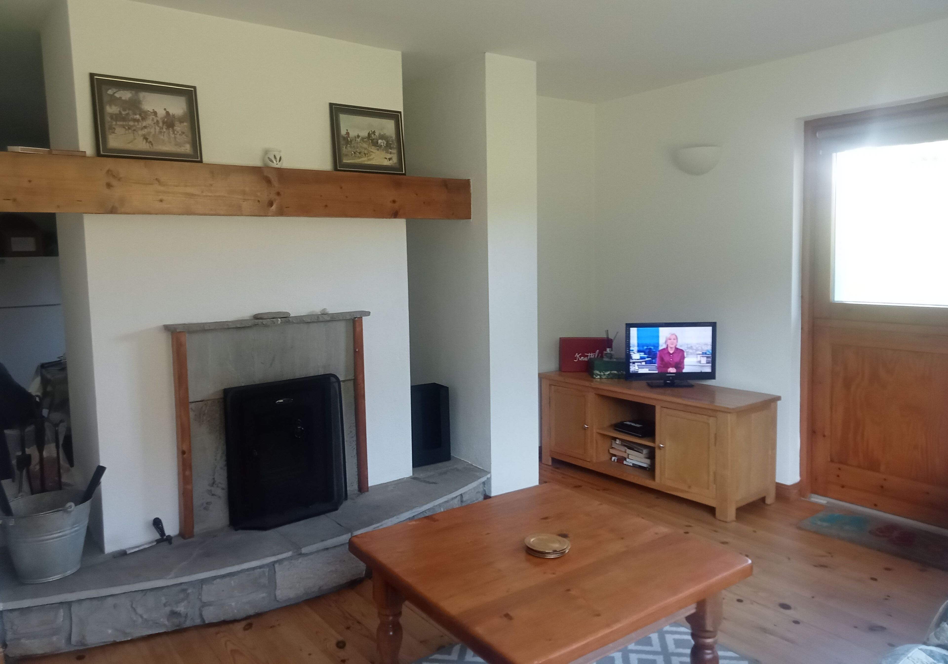 A living room with a fireplace, wooden beams, a television, and a stone fireplace surround.