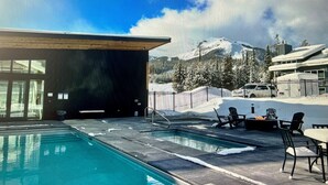 A pool area with a view of snow-covered mountains and a building with large windows.