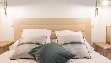 Una cama bien hecha con cabecera, dos mesitas de noche y una lámpara fijada a la pared.