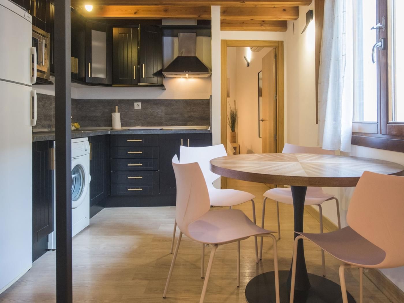 A compact kitchen with dark cabinetry, a built-in washing machine, and a round dining table with chairs.