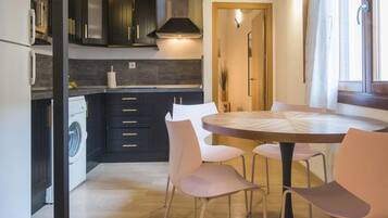 A compact kitchen with dark cabinetry, a built-in washing machine, and a round dining table with chairs.