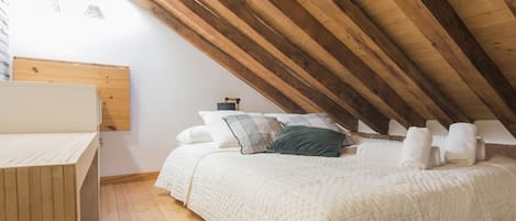 A bedroom with a sloped ceiling, wooden beams, a bed with pillows, a bedside table, and a window.