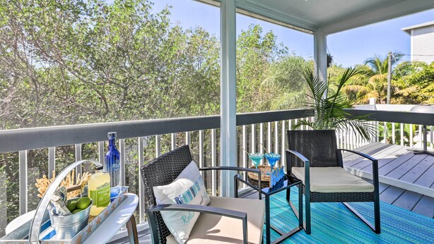 A balcony with wicker chairs, a table with drinks, and a view of trees. - Holmes Beach Retreat: Walk to Beach & Dining! (Holmes Beach)