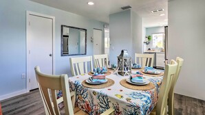 A dining area with a table set for four, white chairs, and a ceiling light fixture. - Holmes Beach Retreat: Walk to Beach & Dining! (Holmes Beach)