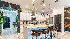 A modern kitchen with a central island, bar stools, pendant lights, and a microwave.
