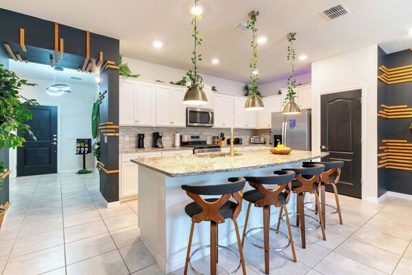 A modern kitchen with a central island, bar stools, pendant lights, and a microwave.