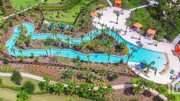 An aerial view of a resort with a winding pool, surrounded by palm trees and lounge areas.