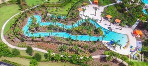 An aerial view of a resort with a winding pool, surrounded by palm trees and lounge areas.