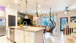 A modern kitchen with white cabinets, a granite countertop, and hanging plants.