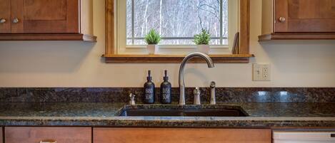 A kitchen with wooden cabinets, a granite countertop, a stainless steel sink, and two potted plants on the windowsill.