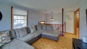 Uma sala de estar com sofá seccional, piso de madeira, um candelabro e uma escada.