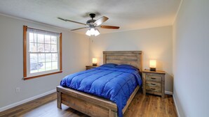 Quarto com cama de madeira, ventoinha no teto, duas mesas de cabeceira com luminárias e uma janela com persianas.