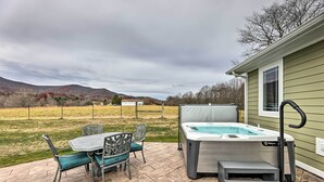 En udendørs terrasse med jacuzzi, et bord med stole og udsigt til en græsplæne og bjerge.