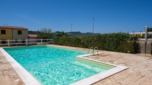 Una piscina rettangolare con acqua cristallina, circondata da un solarium piastrellato e una recinzione bianca.