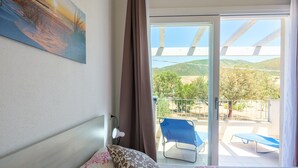 Una camera d'albergo con un letto, un quadro, una tenda e un balcone con una sedia e un tavolo.