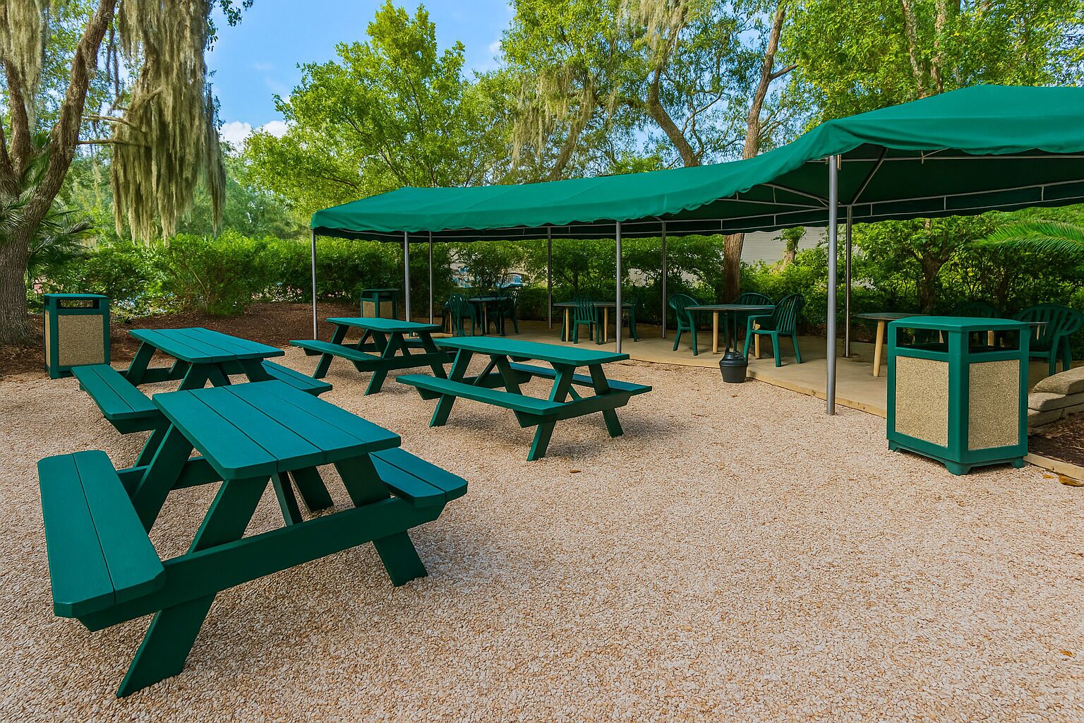 Un espace extérieur aménagé avec des tables et des bancs de pique-nique verts, entouré d’arbres et recouvert d’une pergola verdoyante.