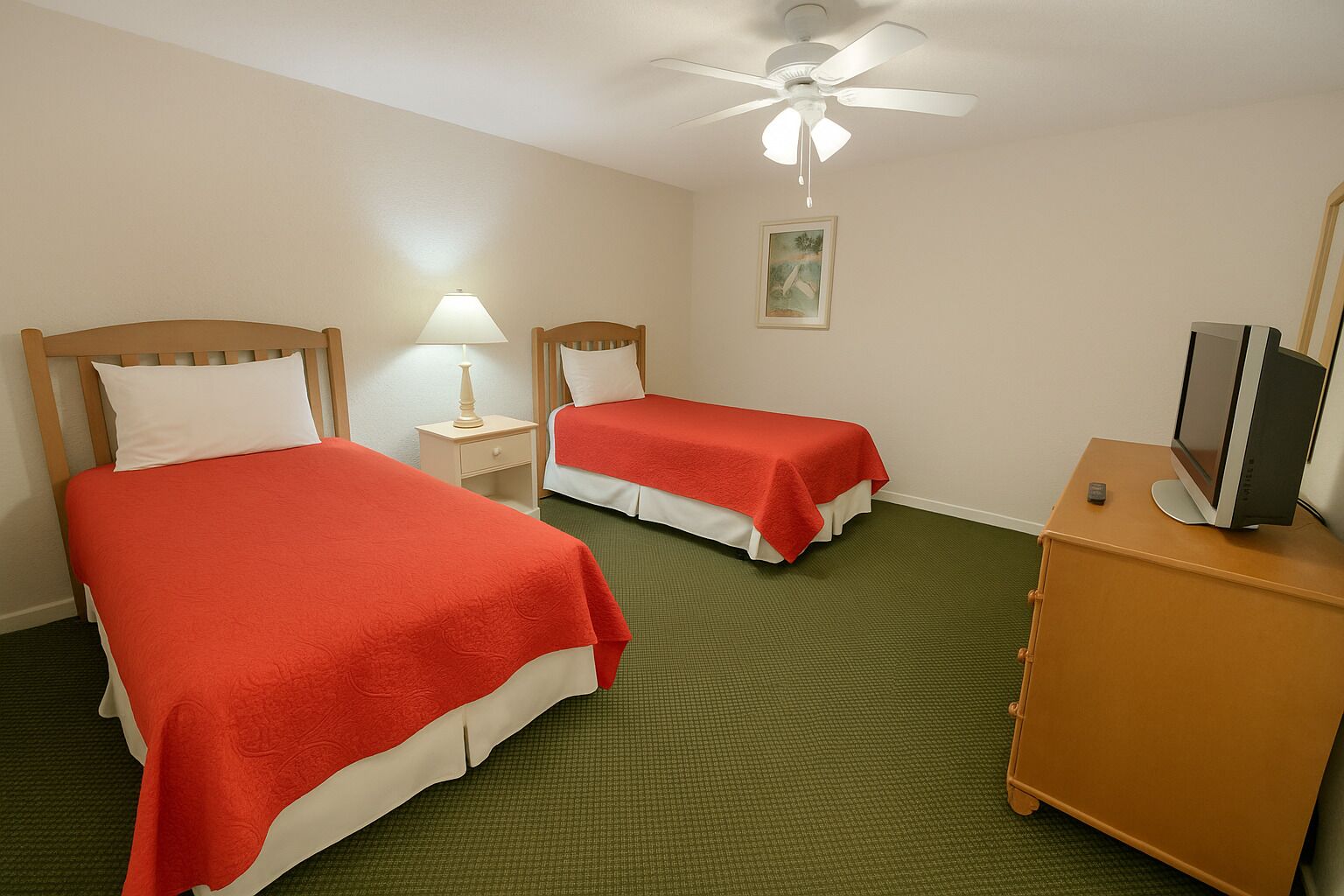 A hotel room with two beds, a ceiling fan, a TV on a cabinet, and a framed picture on the wall.