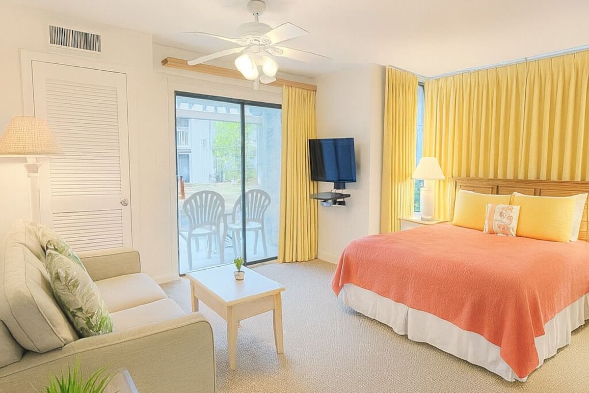 Habitación de hotel con cama, sofá, una mesita, televisión y balcón con sillas.