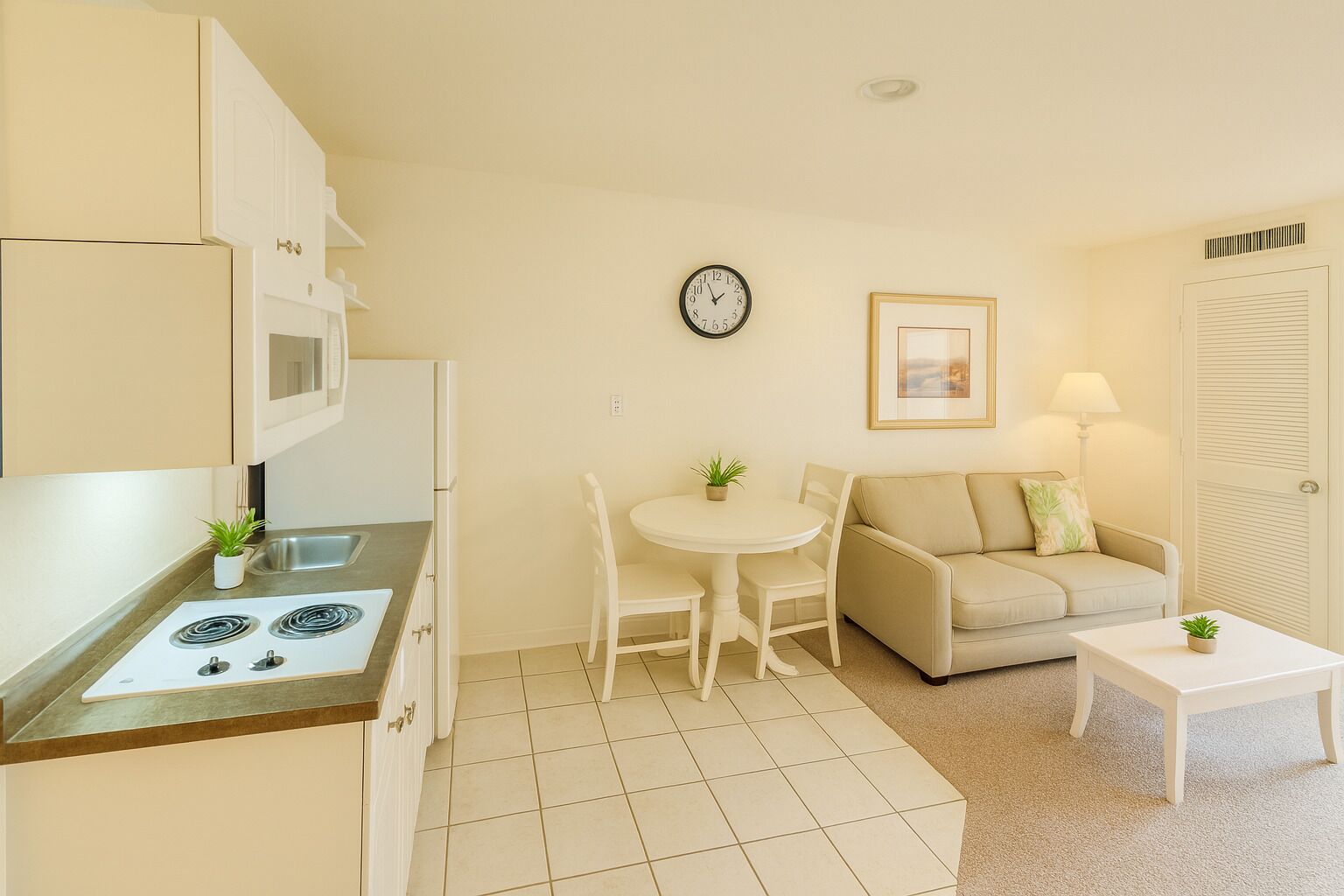 A compact kitchen with a stove, sink, and cabinets, a dining table with chairs, a sofa, and a small coffee table.