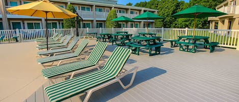 A deck with green-striped lounge chairs and picnic tables, surrounded by a white picket fence.