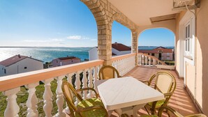 Un balcón con mesa y sillas blancas, con vistas a la costa.