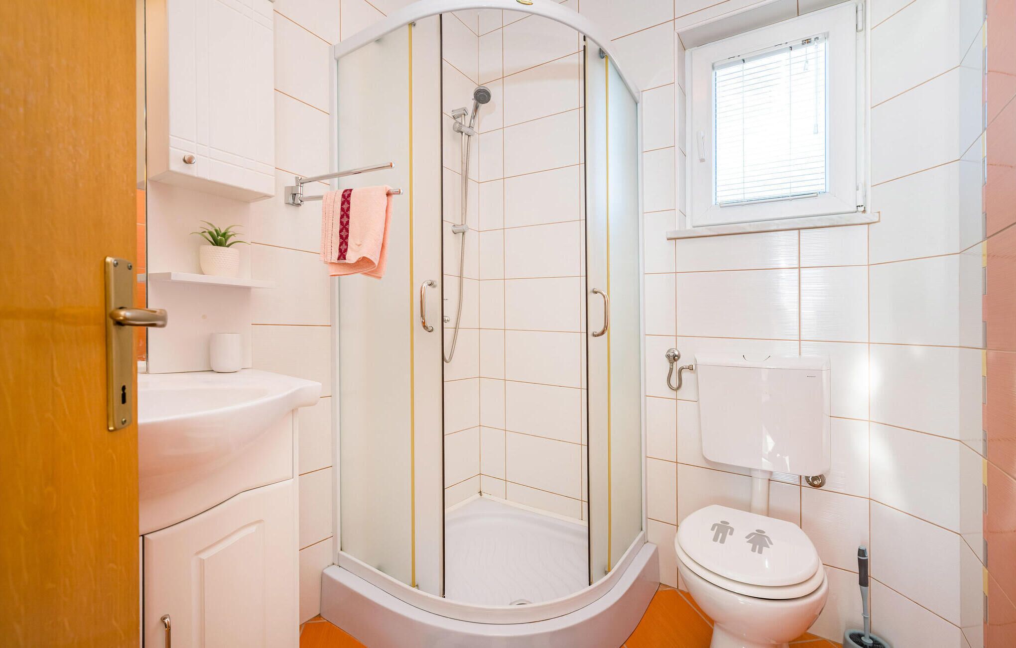 Une salle de bain avec une douche, des toilettes, un lavabo et une petite fenêtre.