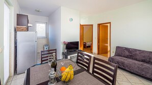 Un espacio habitable compacto con zona de comedor, sofá, televisión y kitchenette.