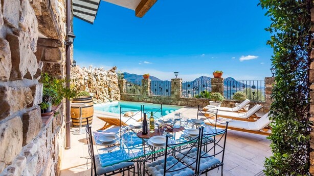 Área de piscina no terraço, com mesa posta para refeições, cadeiras de descanso e uma parede de pedra.