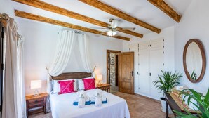 Quarto com cama, luminárias de cabeceira, ventoinha no teto, porta de madeira e espelho.