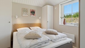 Un dormitorio con una cama, dos lámparas fijadas a la pared, un ventanal con vistas a la vegetación y dos grabados botánicos enmarcados.