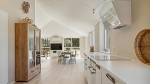 Una cocina moderna con techo alto, comedor con mesa y sillas, y un ventanal que proporciona luz natural.