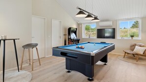 Una mesa de billar con bolas, una televisión y una máquina de juegos en una habitación con piso de madera y techo alto.