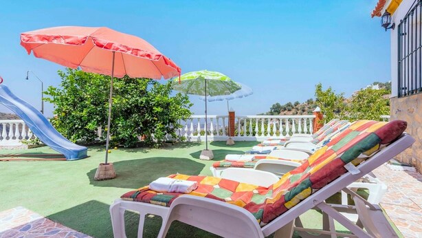 A poolside area with lounge chairs, a slide, and umbrellas. - Villa Marín Canillas de Aceituno by Ruralidays (Málaga)