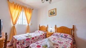 A room with two wooden beds, a window with curtains, a bedside table with a lamp, and a wall-mounted picture. - Villa Marín Canillas de Aceituno by Ruralidays (Málaga)
