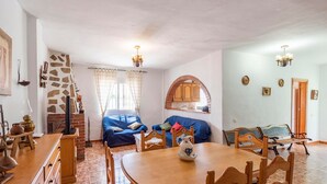A cozy living room with a blue sofa, a wooden dining table, and a kitchen area with a brick oven. - Villa Marín Canillas de Aceituno by Ruralidays (Málaga)