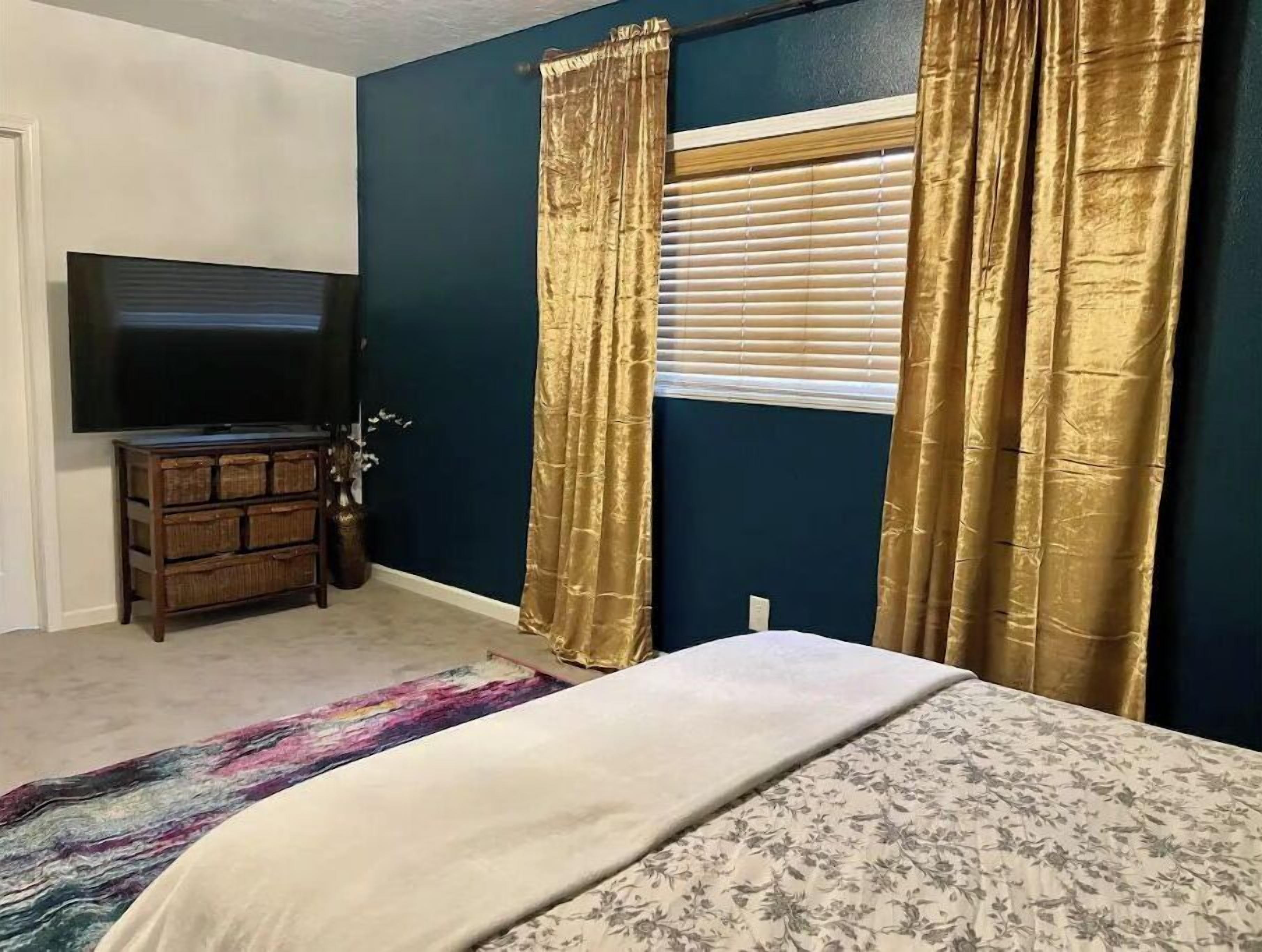 A bedroom with a bed, a dresser, a television, and a window with curtains.