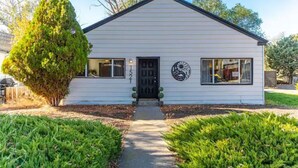 A single-story house with a black door and windows, surrounded by well-maintained lawns and a tree. - Heart of Bend-Walkable, Ping Pong, Billards (Bend)