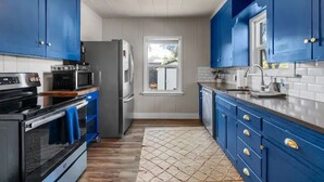A modern kitchen with blue cabinets, stainless steel appliances, and a large window. - Heart of Bend-Walkable, Ping Pong, Billards (Bend)