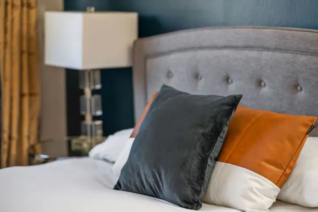 A bed with a tufted headboard, two pillows, and a bedside lamp.