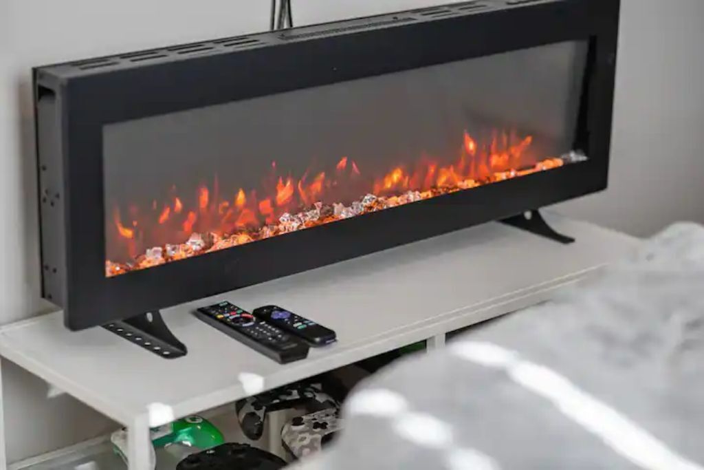 Un televisor de pantalla plana con una chimenea decorativa, un mueble blanco para entretenimiento y un control remoto.