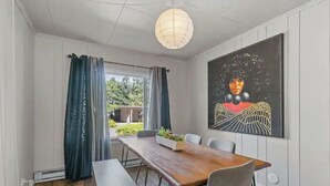 A dining area with a wooden table and chairs, a bench, a large painting on the wall, and a view of greenery outside. - Heart of Bend-Walkable, Ping Pong, Billards (Bend)