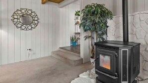 A cozy room with a wood-burning stove, white walls, a wooden ceiling, and a potted plant. - Heart of Bend-Walkable, Ping Pong, Billards (Bend)